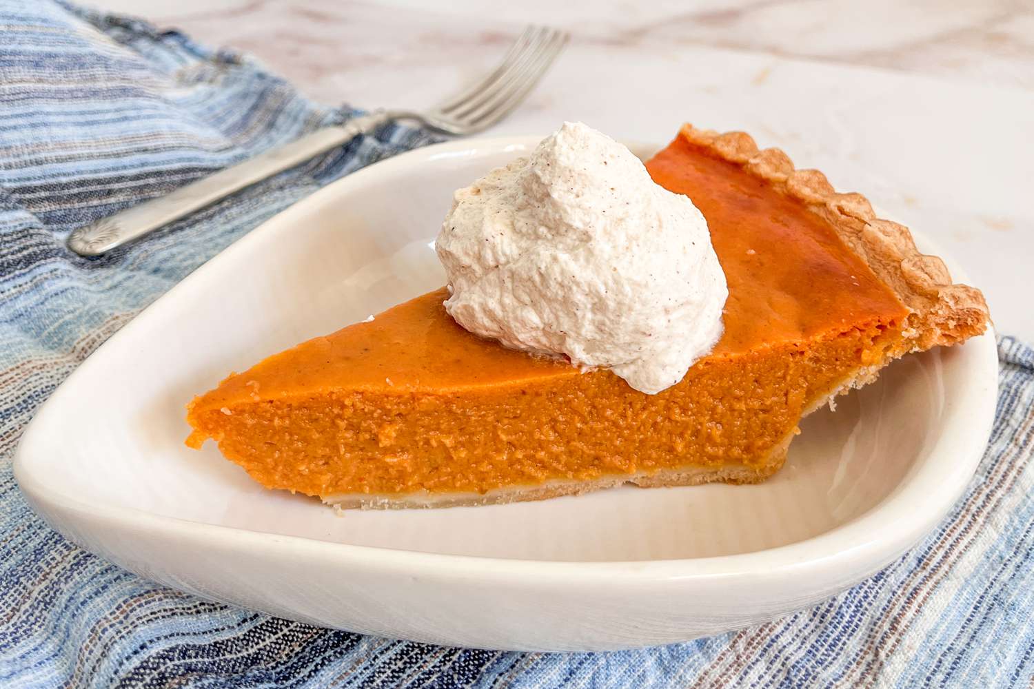 Slice of pumpkin pie on a plate with a dollop of cinnamon whipped cream