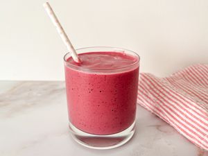 A short glass filled with a pink smoothie and a white paper straw with light pink polka dots