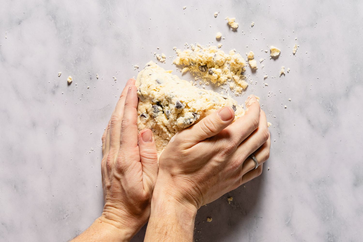 Hands kneading dough with chocolate chips on a marble surface for Chocolate Chip Scones recipe