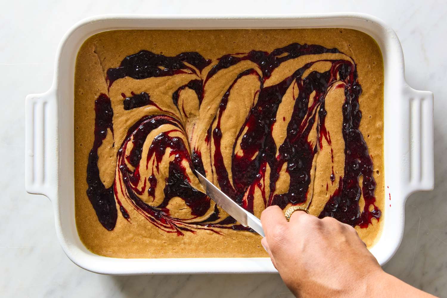 Jam getting swirled into cake batter in a white baking dish for the Easy Jam Cake recipe