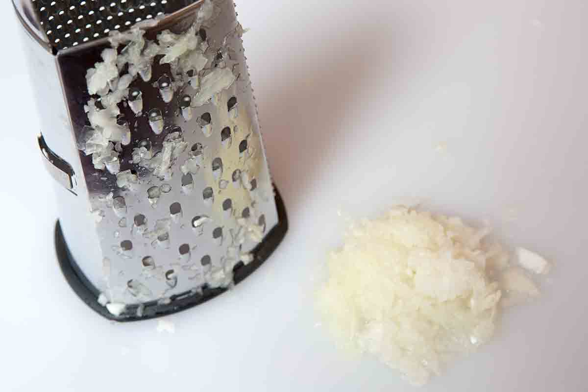 Grated onion next to a box grater resting on a white surface