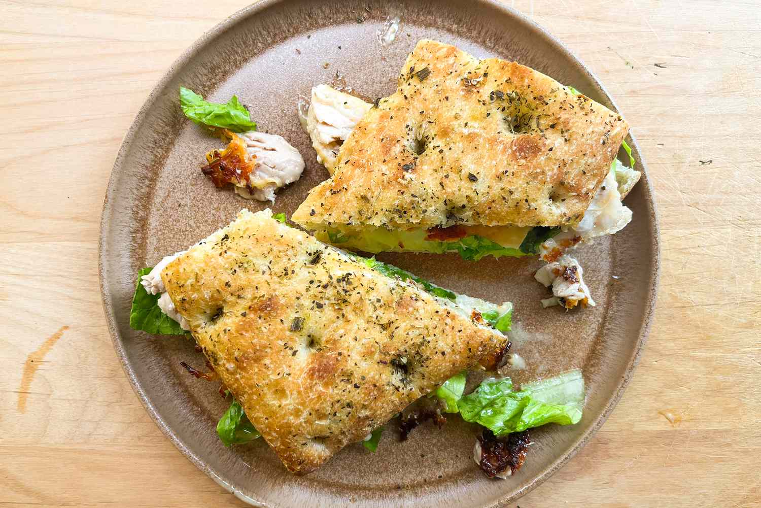 A sandwich made with focaccia bread on a plate cut in half with visible ingredients like lettuce and sundried tomatoes