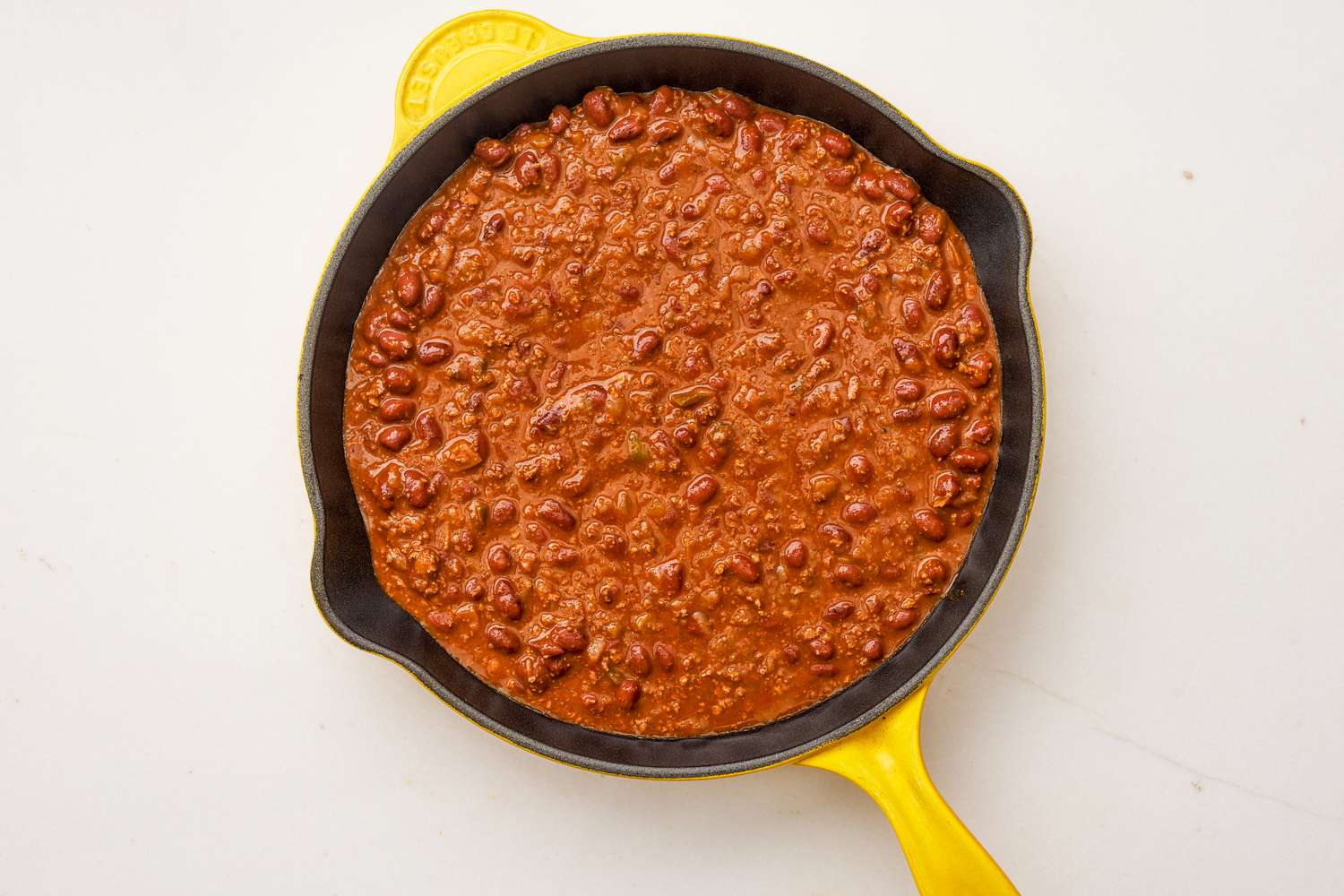 Canned chili added to the cast iron skillet for frito pie dip recipe