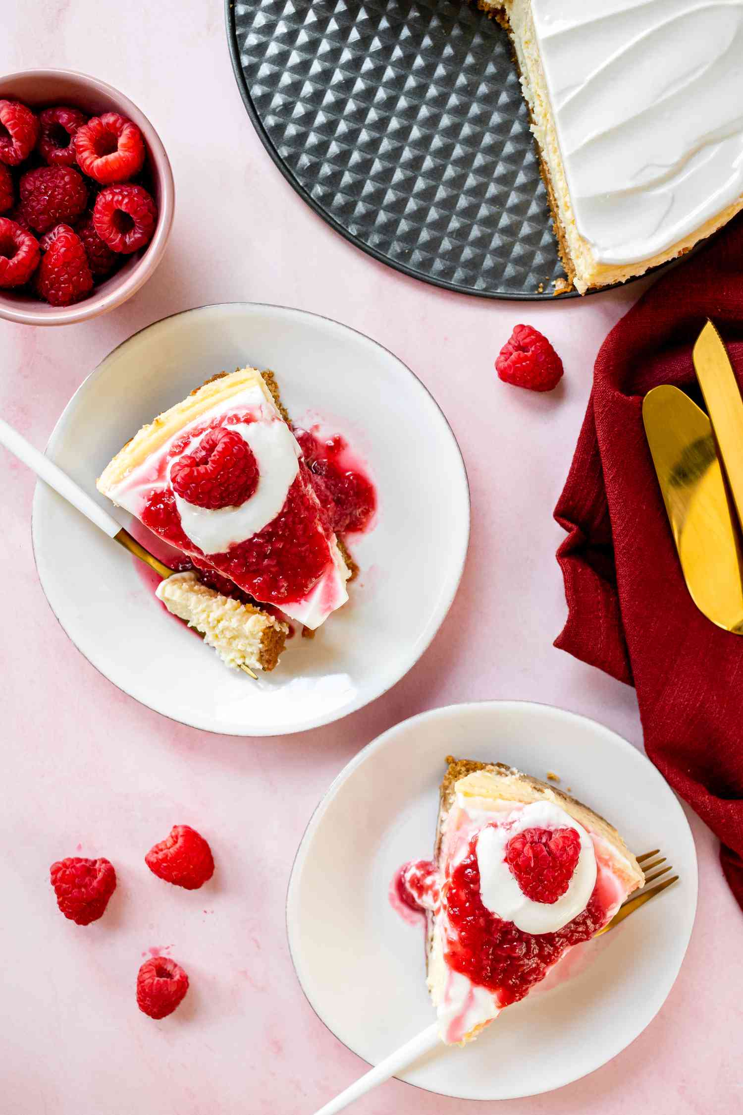 Overhead view of two plates with raspberry topped New York cheesecake with raspberries set around the plates.