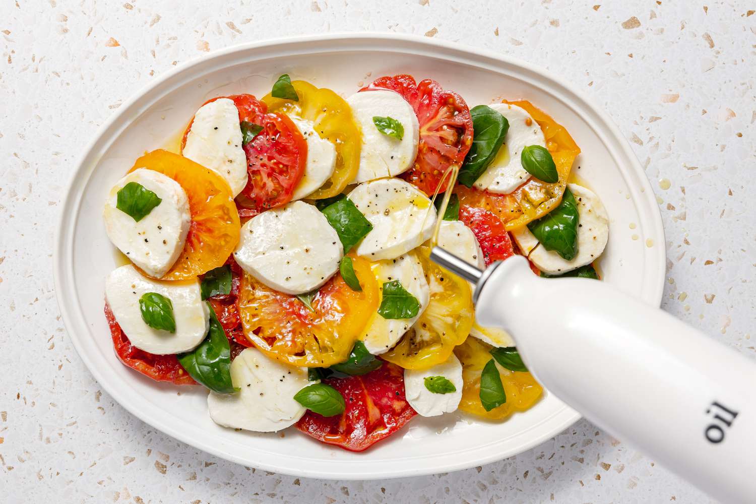 Olive Oil Drizzled Onto Caprese Salad With Tomatoes, Basil, and Mozzarella Topped With Cracked Pepper 