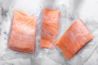 Three frozen salmon fillets in packaging on the counter