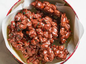 Chocolate candy clusters with nuts and sprinkles in a container lined with paper