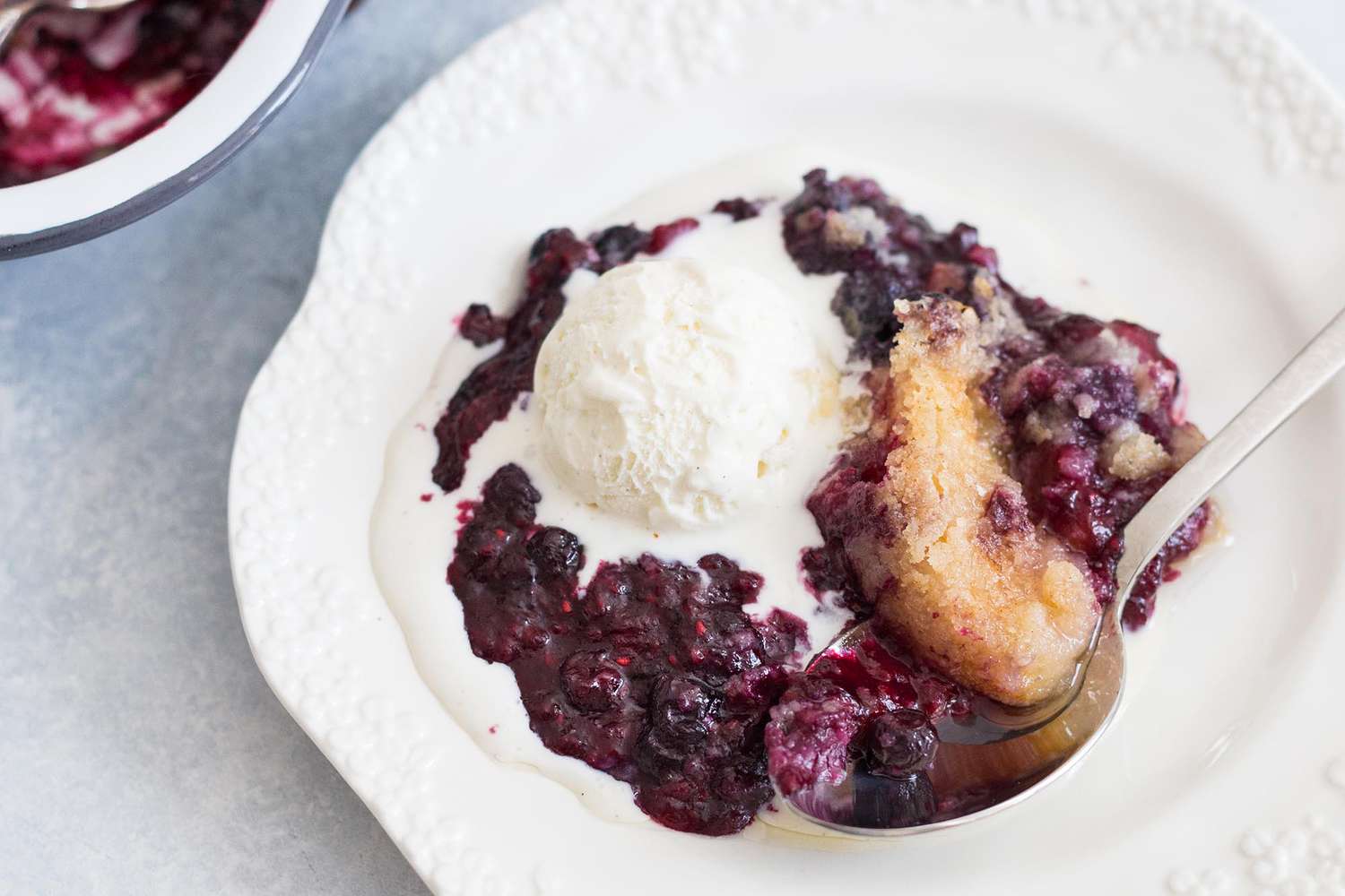 Peach Dump cake recipe plated dump cake with scoop of vanilla ice cream in a white bowl