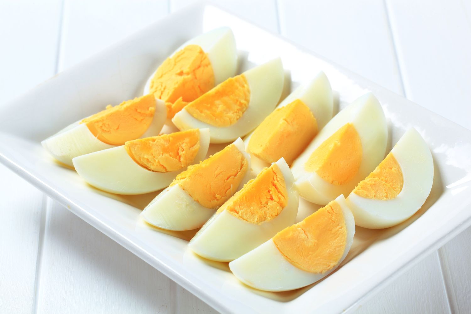 Ten slices of hardboiled eggs on a tray on a white tabletop