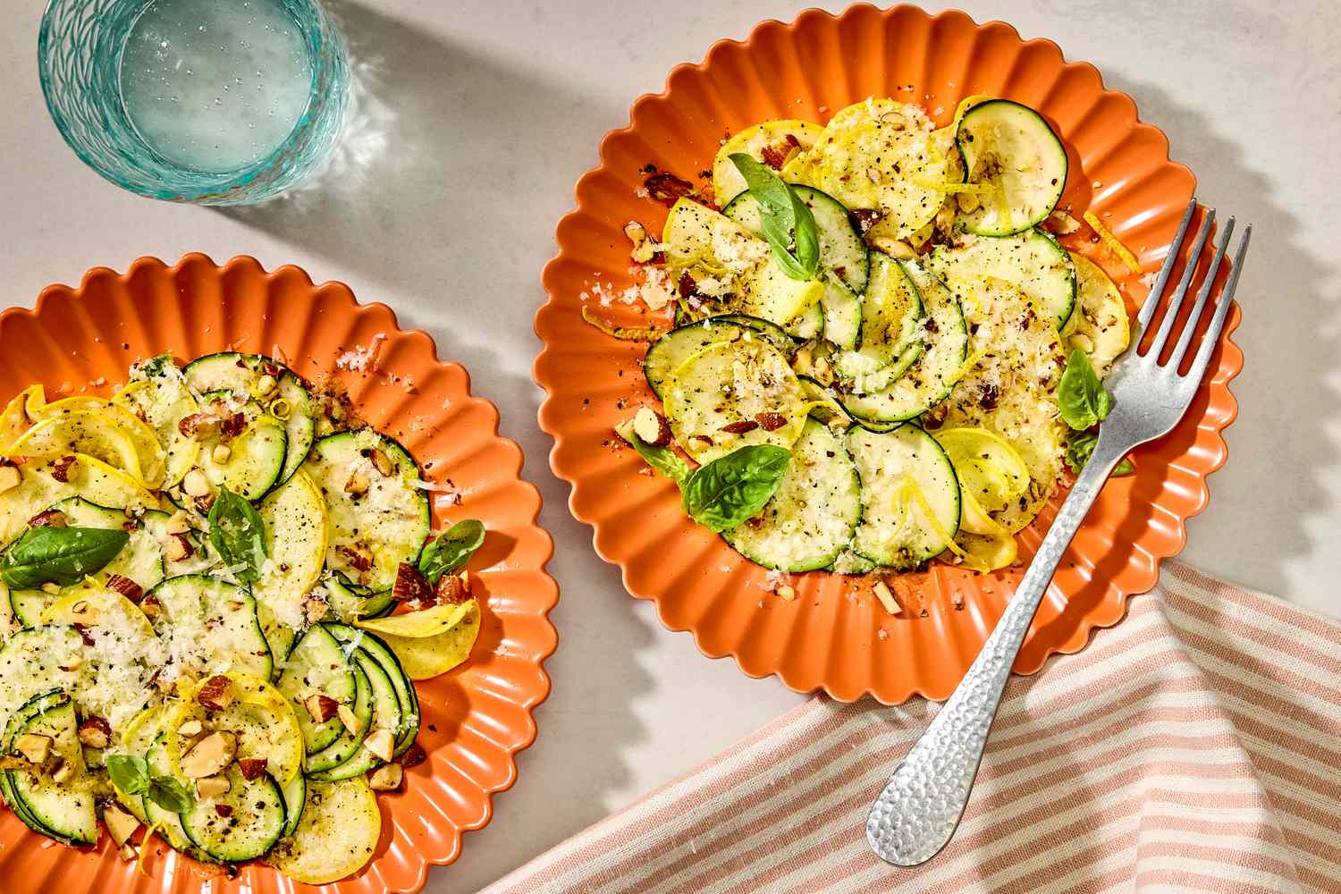 Two plates of summer squash salad with a fork placed near a striped napkin