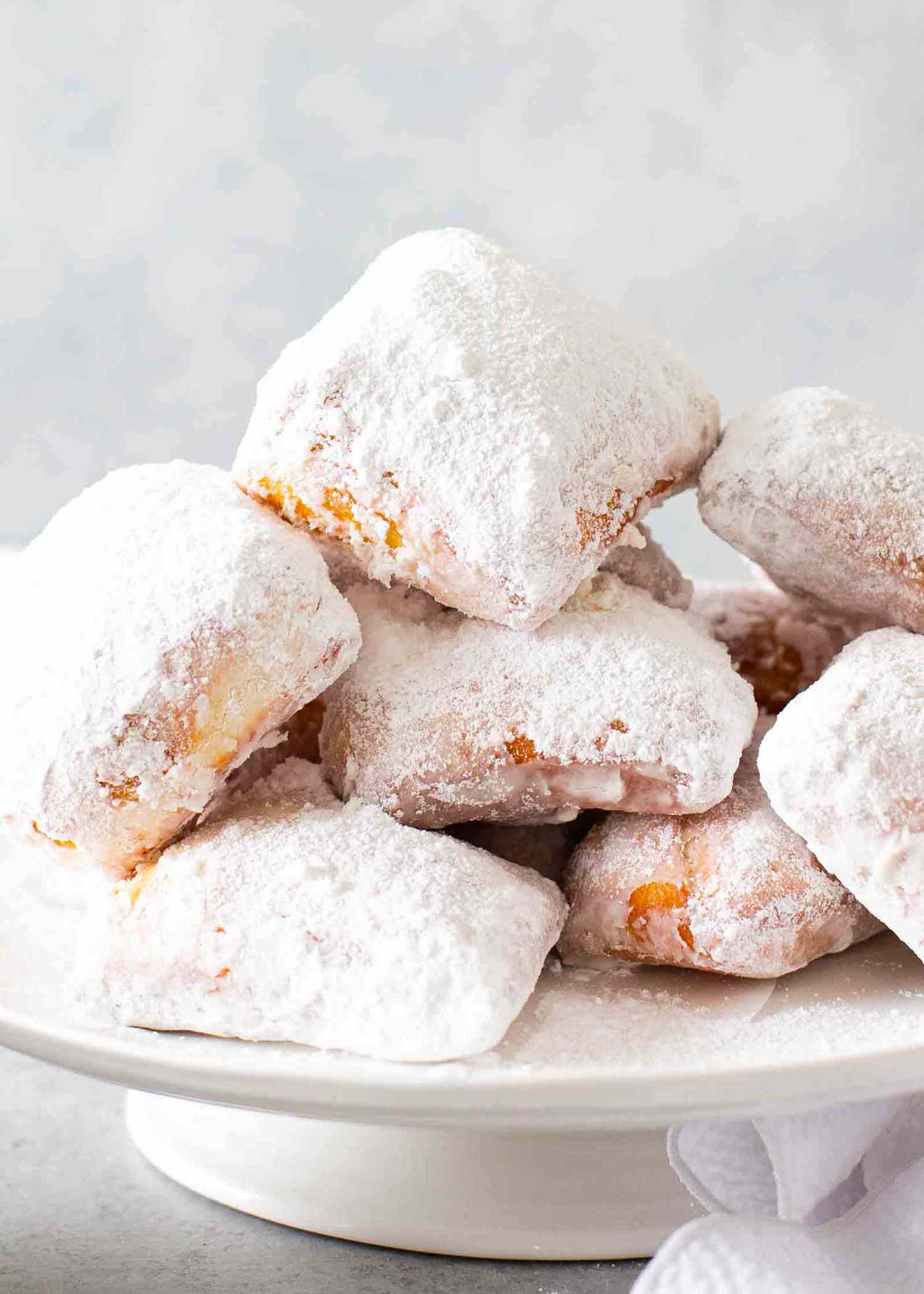 New Orleans Beignets stacked on a cake plate with two cups of espresso visible to the left and a paper towel to the right.
