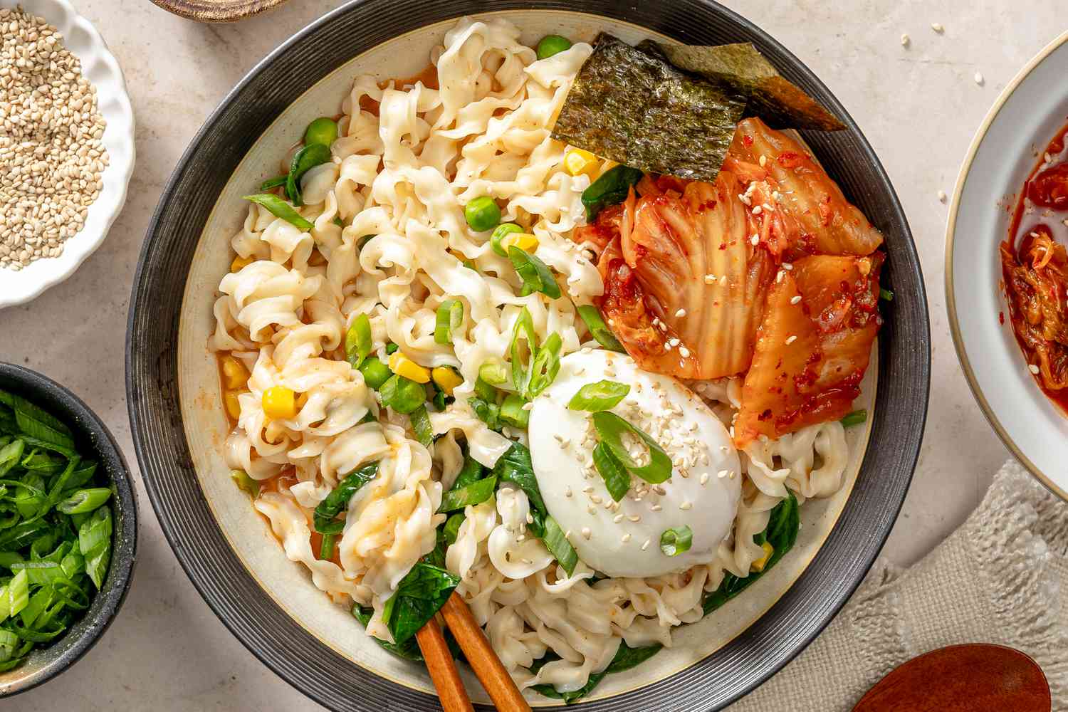 Noodle bowl dish with a soft-boiled egg, vegetables, kimchi, and chopsticks, served in a black bowl, garnished decoratively
