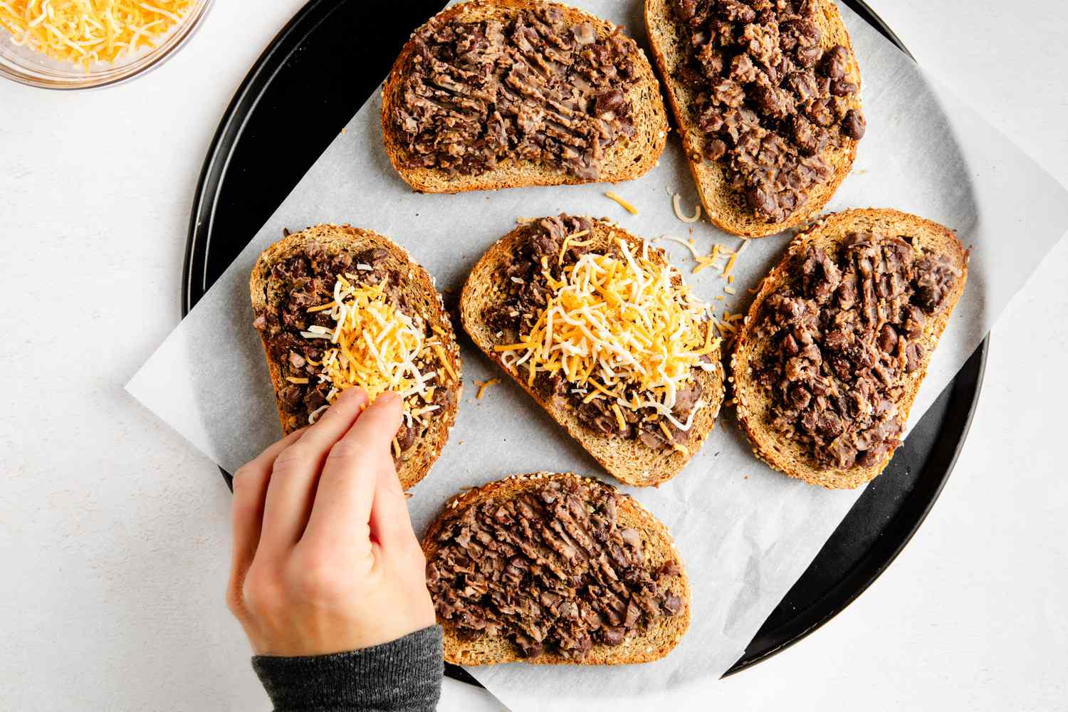 Black bean toast topped with shredded cheese on a parchment paper lined platter