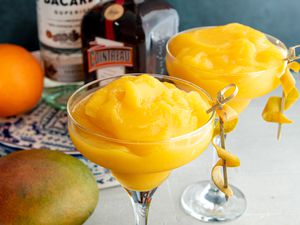 Frozen mango daiquiris in martini glasses garnished with curled mango peel.