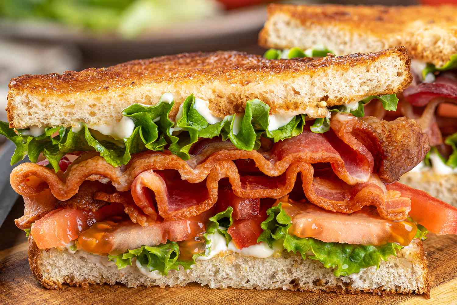 Closeup of a BLT sandwich with bacon, lettuce, tomato, and mayonnaise, on toasted bread slices, prepared and presented on a wooden surface