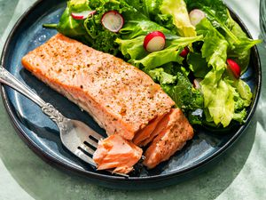 Mayo salmon fillet with a side green salad on a plate, with a fork having picked into one side of the salmon