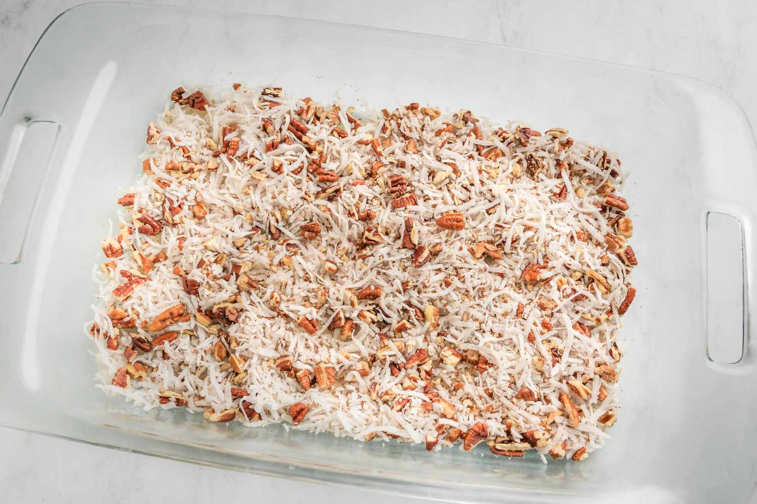 chopped pecan and shredded coconuts in a pyrex dish for earthquake cake recipe