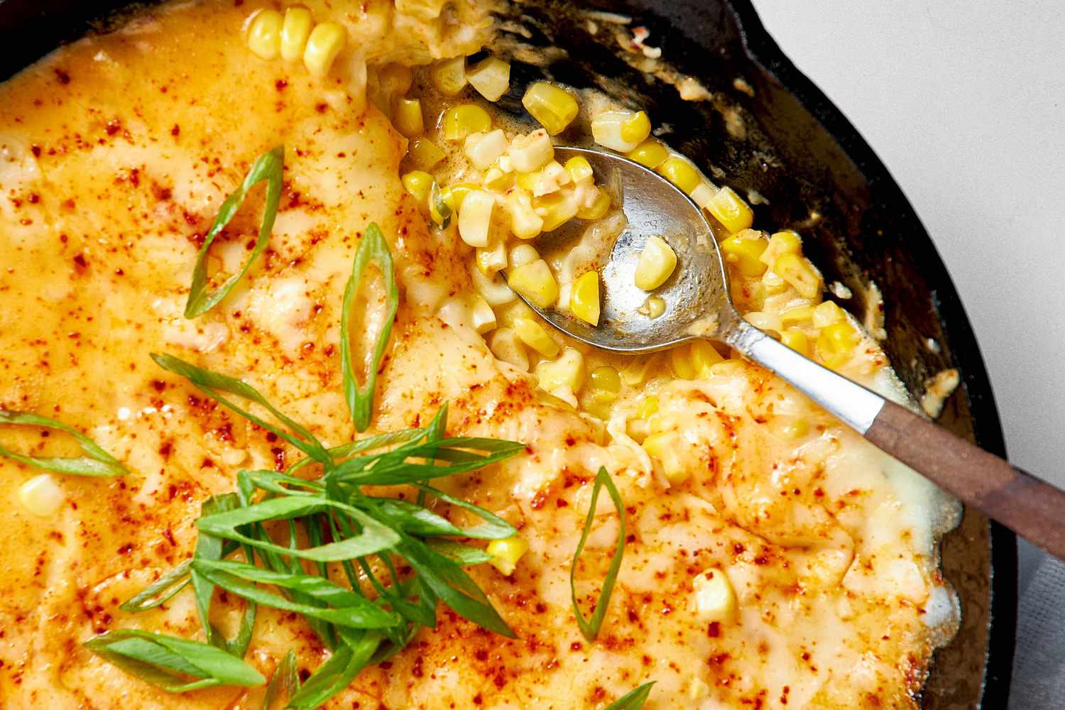 Close-up: Cast Iron Skillet With Korean Corn Cheese Topped With Sliced Green Onions and a Spoon (After Some of the Korean Cheese Corn Was Served)