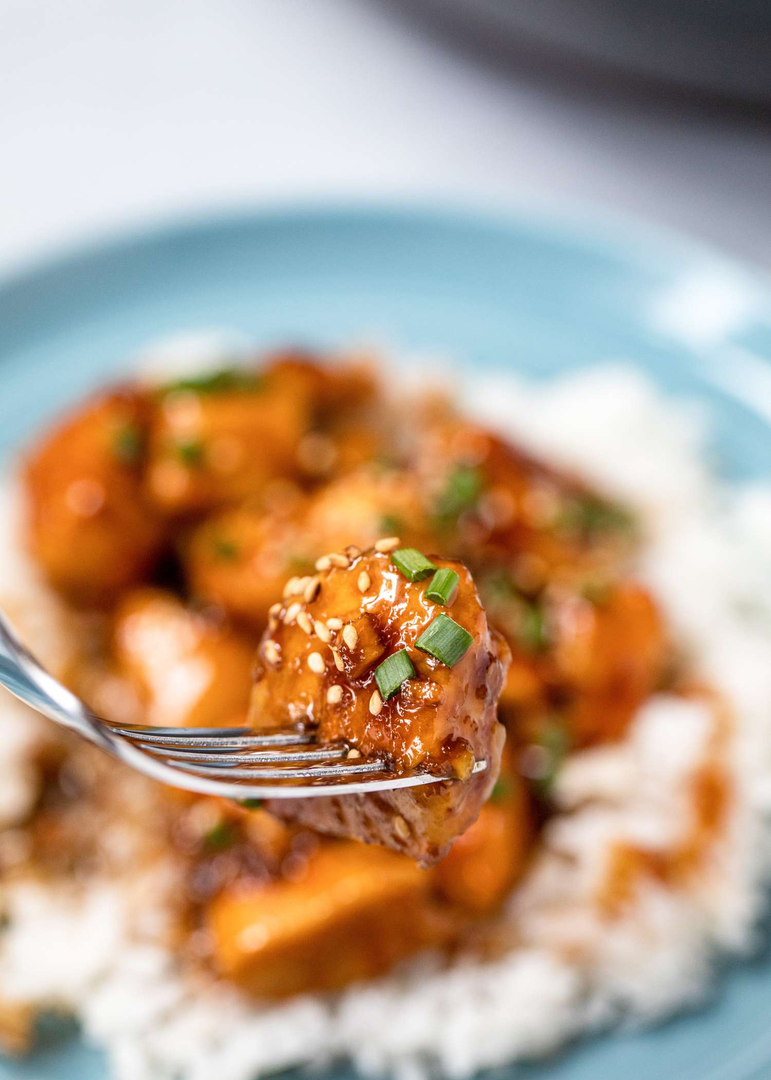 Side view of a fork lifting a piece of Sweet and Tangy Bourbon Chicken.