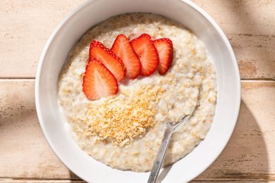Coconut oatmeal topped with sliced strawberries and toasted coconut, served in a bowl with a spoon.