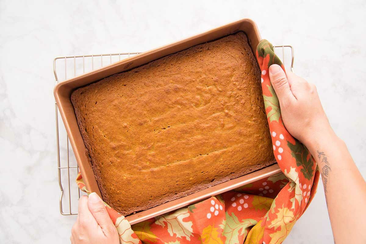 Pumpkin Snack Cake in a pan and held above a cooling rack.