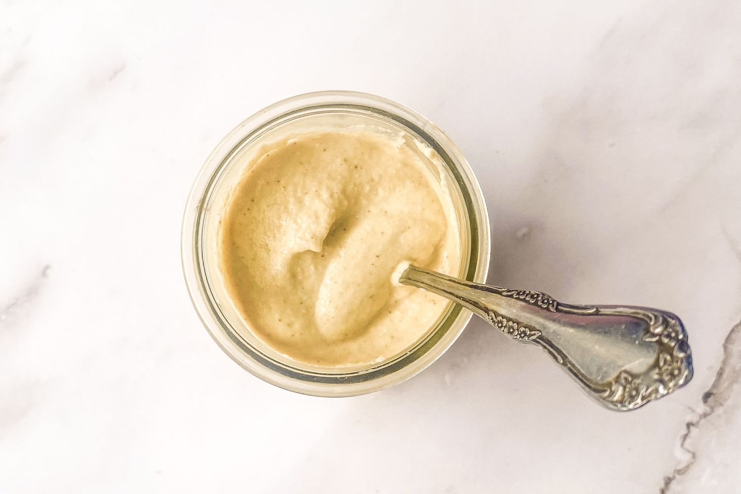 Jar of cashew dressing with a spoon placed inside.