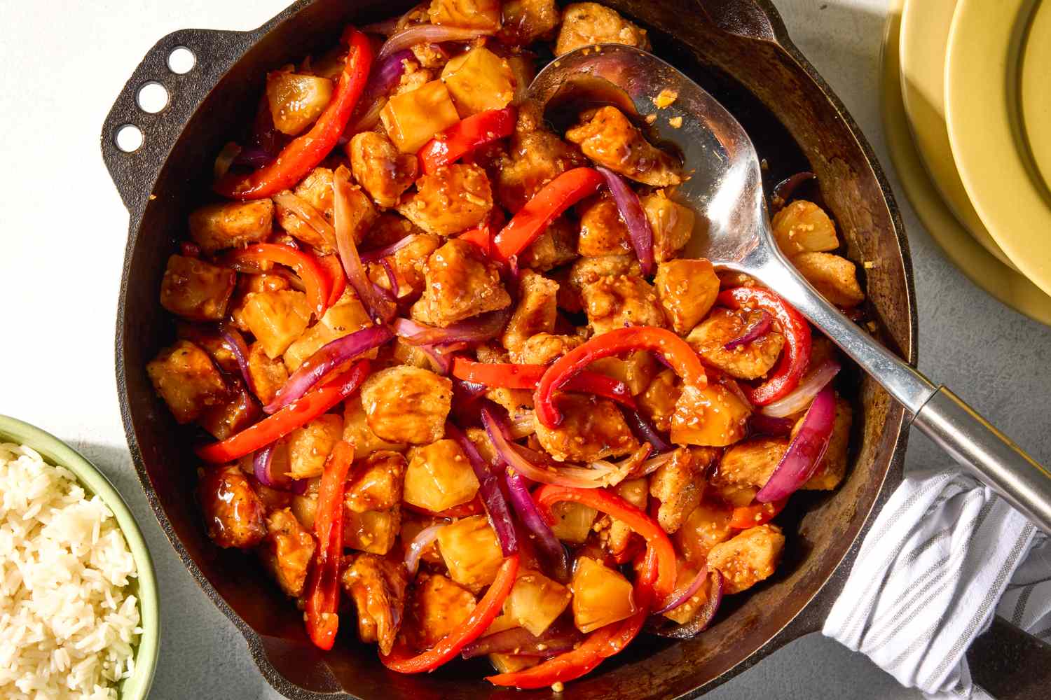 A skillet containing a dish with chunks of chicken pineapple and bell peppers in a sauce