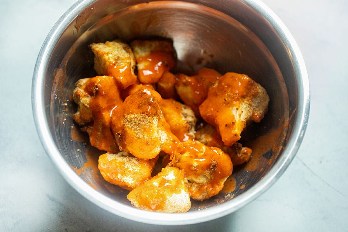 Air Fryer Buffalo Cauliflower Bites in a metal bowl with sauce poured on top.