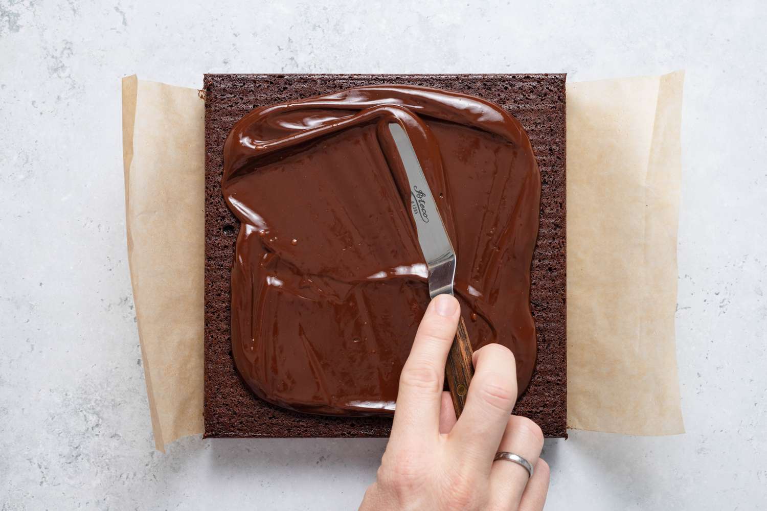 Offset spatula used to spread ganache on the brownie on a parchment paper