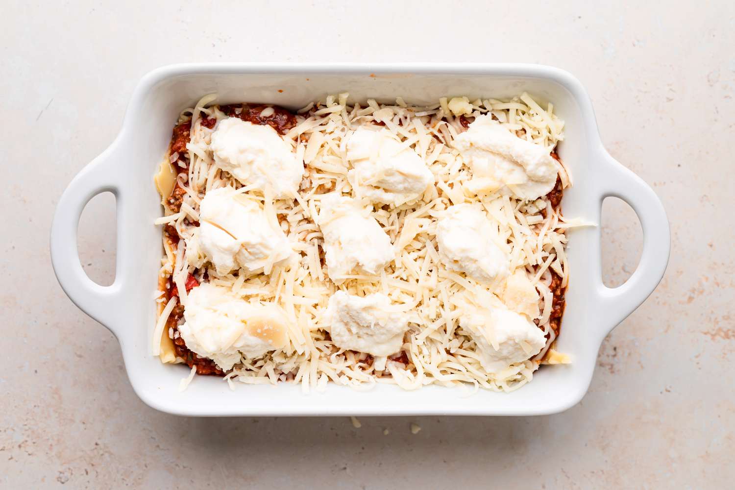 Dolloping ricotta over shredded cheese to make the best lasagna recipe.