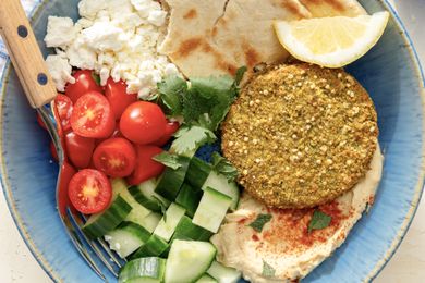 overhead view of Falafel Bowl - pita, feta, falafel, hummus, lemon slice, cucumbers, and grape tomatoes