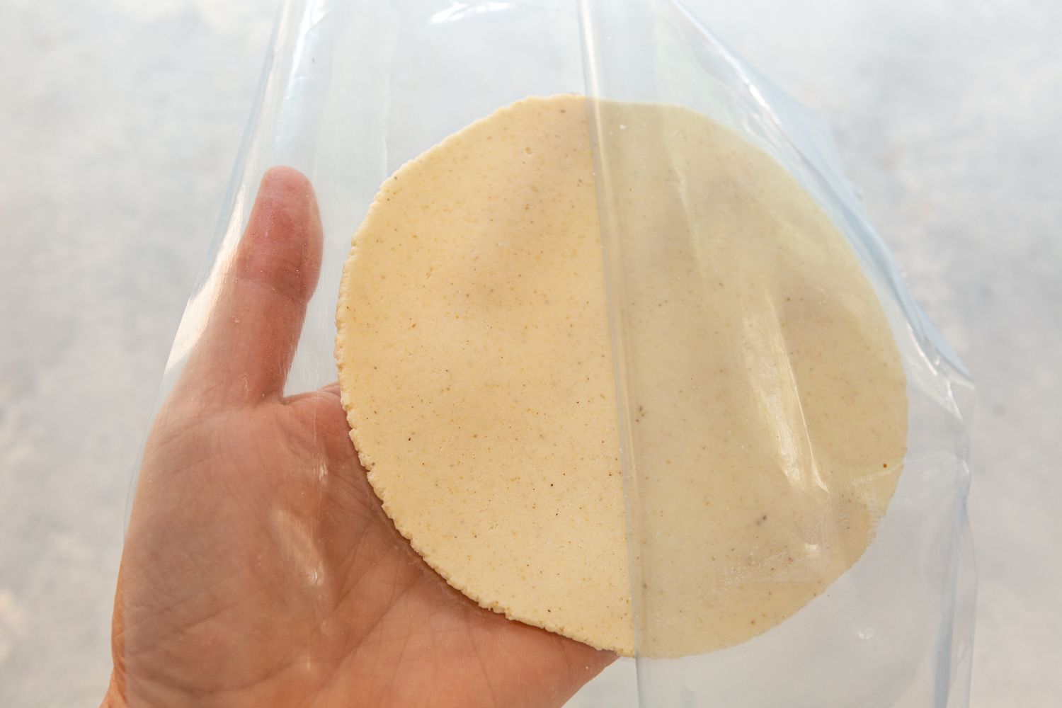 Holding a pressed tortilla a removing the plastic on top 