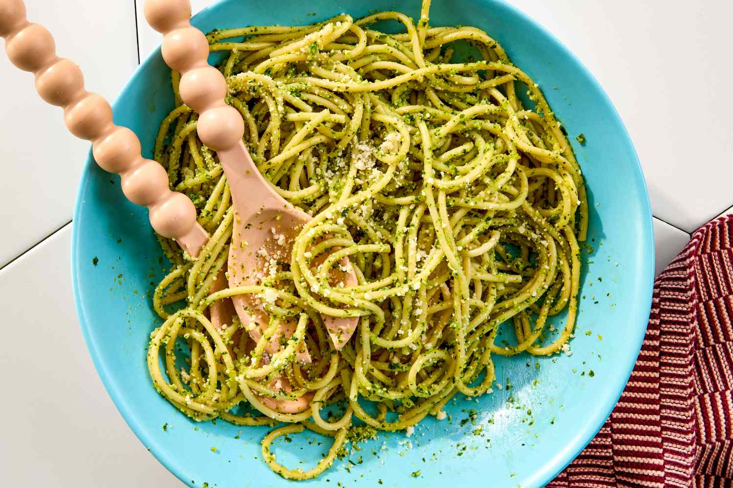 A bowl of pasta with pesto sauce and a wooden spoon served in a blue dish placed on a table