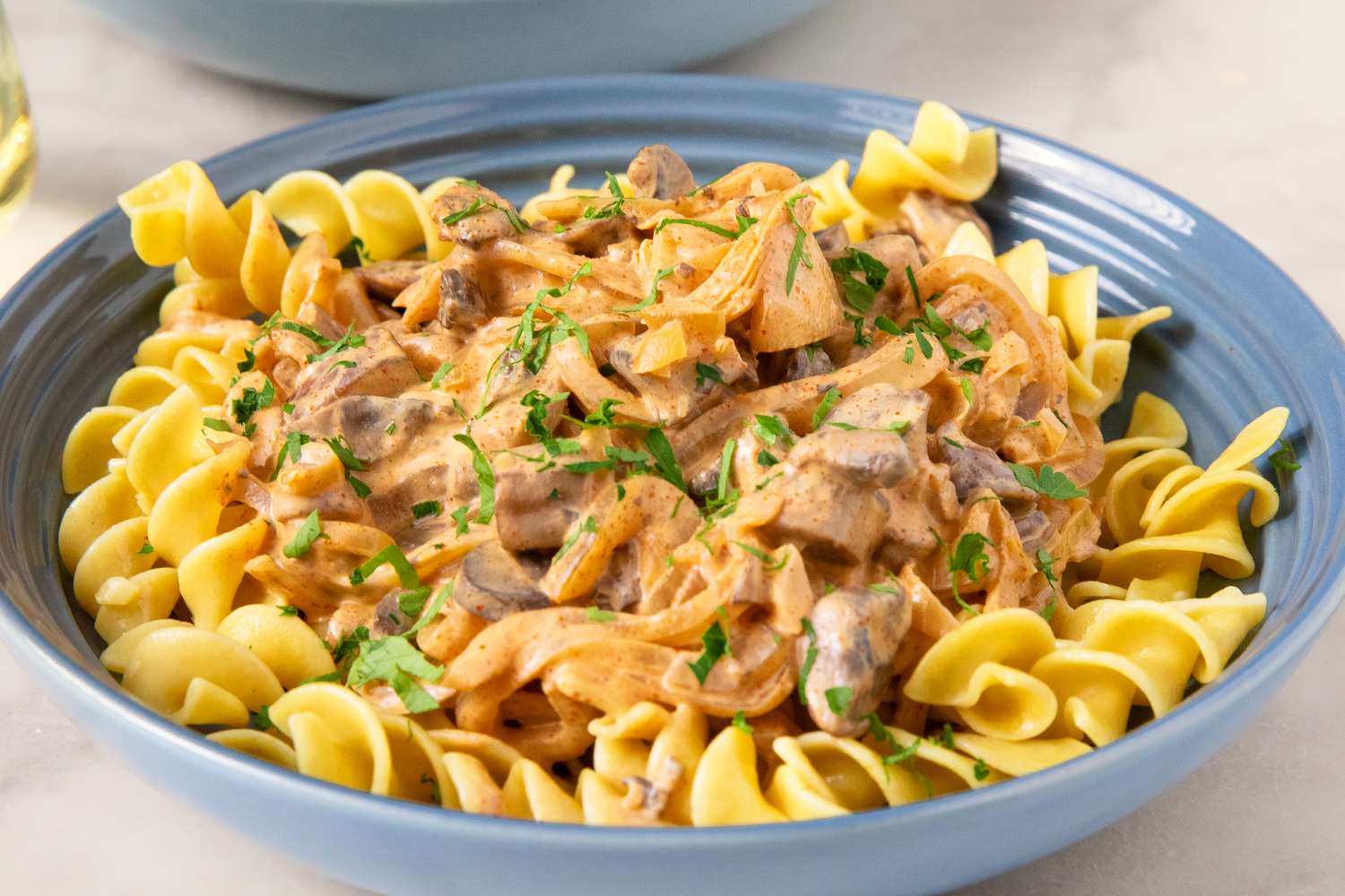 A plate of mushroom stroganoff served over a bed of pasta garnished with parsley