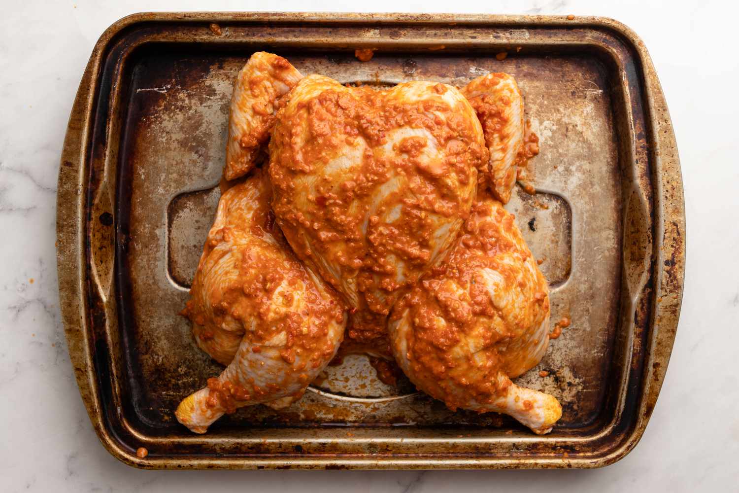 Marinate Spatchcock Chicken in Harissa Butter on a Baking Sheet for Smoked Spatchcock Chicken with Harissa Butter and Grilled Carrots