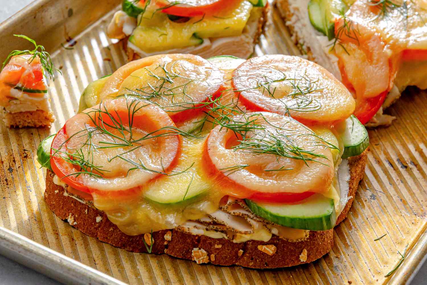 Openfaced sandwich with layers of sliced tomatoes cucumbers melted cheese and garnished with herbs served on a tray