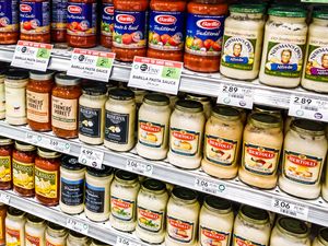 Shelves of jarred pasta sauces in a supermarket featuring brands like Barilla Raos and Bertolli arranged neatly