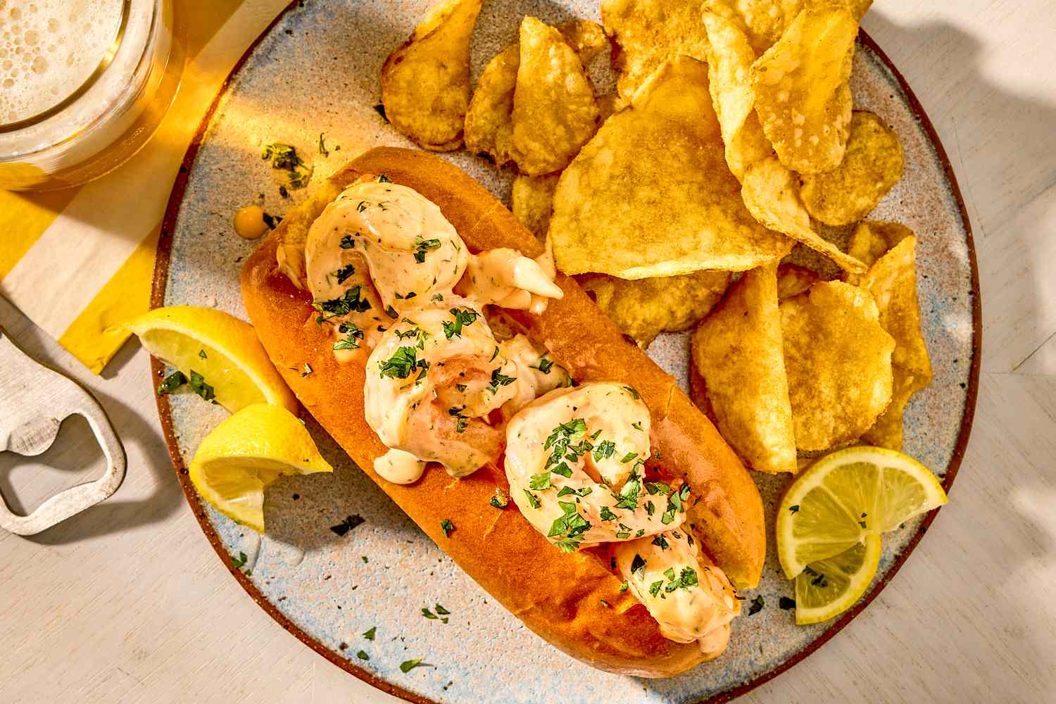 A shrimp roll on a plate accompanied by potato chips and lemon slices