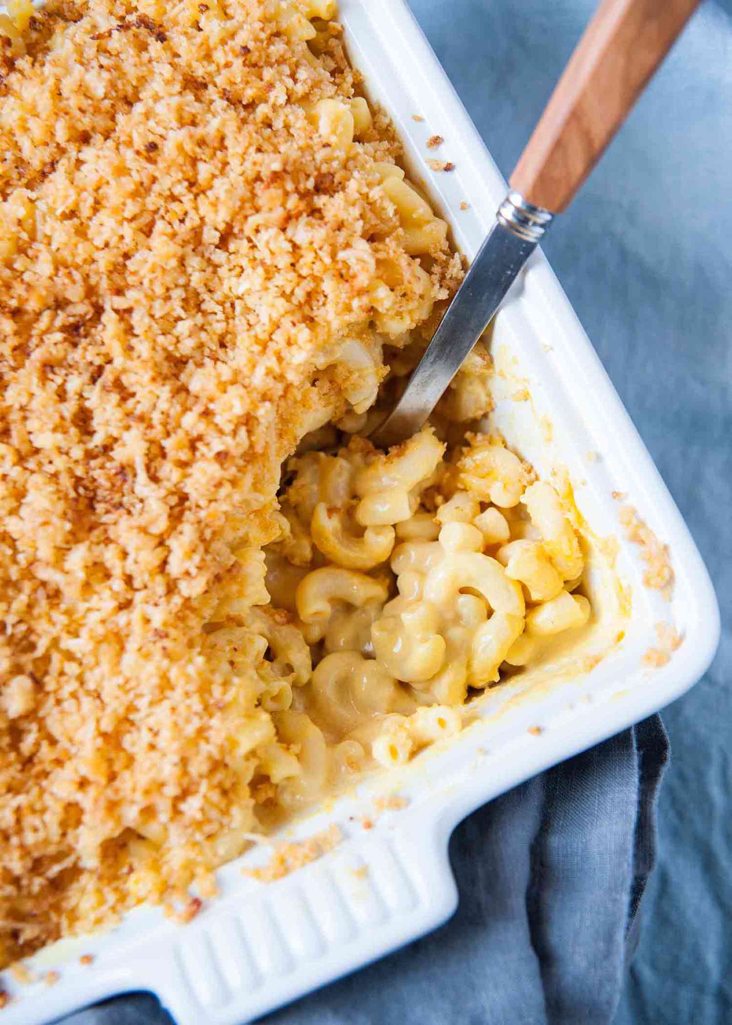 How to make mac and cheese - white casserole dish filled with macaroni and cheese - white casserole dish with filled with mac and cheese. A scoop is taken out