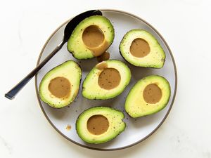 Halved avocados with dressing in their pits served on a plate with a spoon