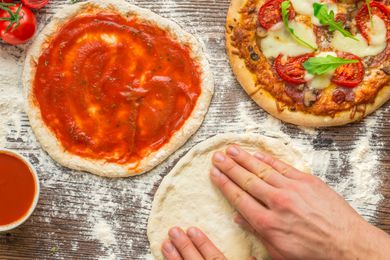 someone forming pizza dough on a counter next to a pizza topped with tomato sauce and a baked pizza 