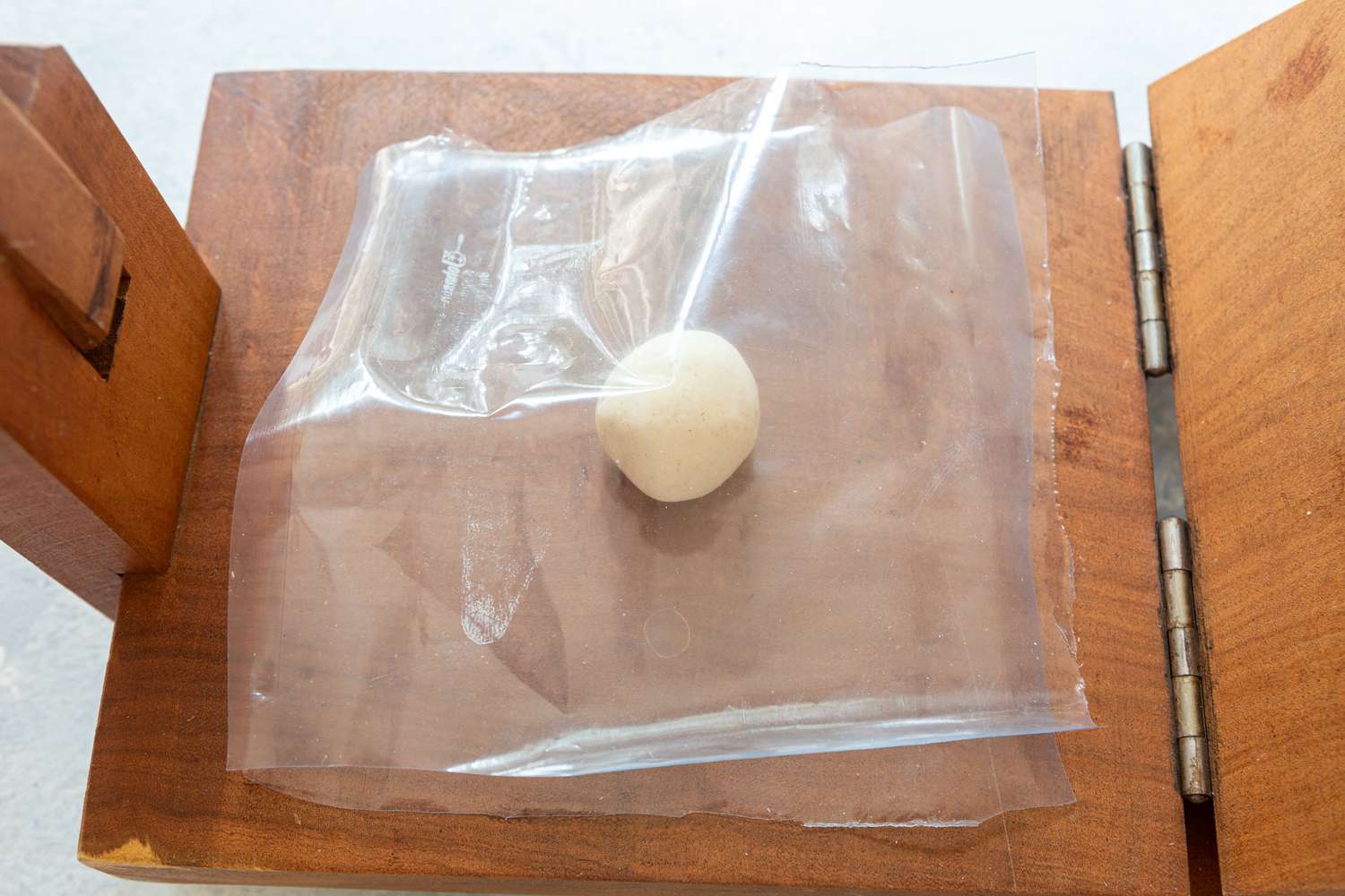 A dough ball covered in plastic on a tortilla press