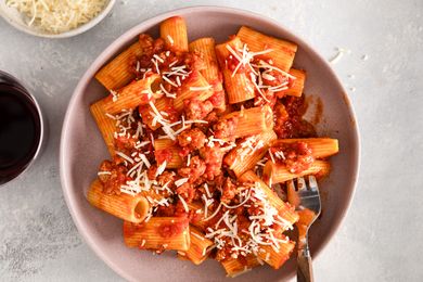 Rigatoni pasta topped with sausage tomato sauce and shredded cheese served on a plate with a fork