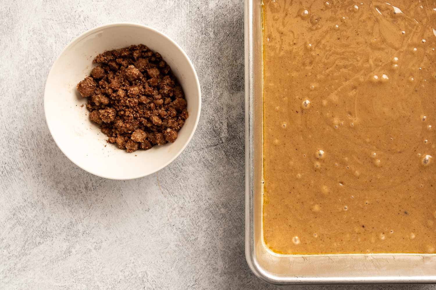 A bowl of crumb topping and a baking pan with uncooked coffeecake batter