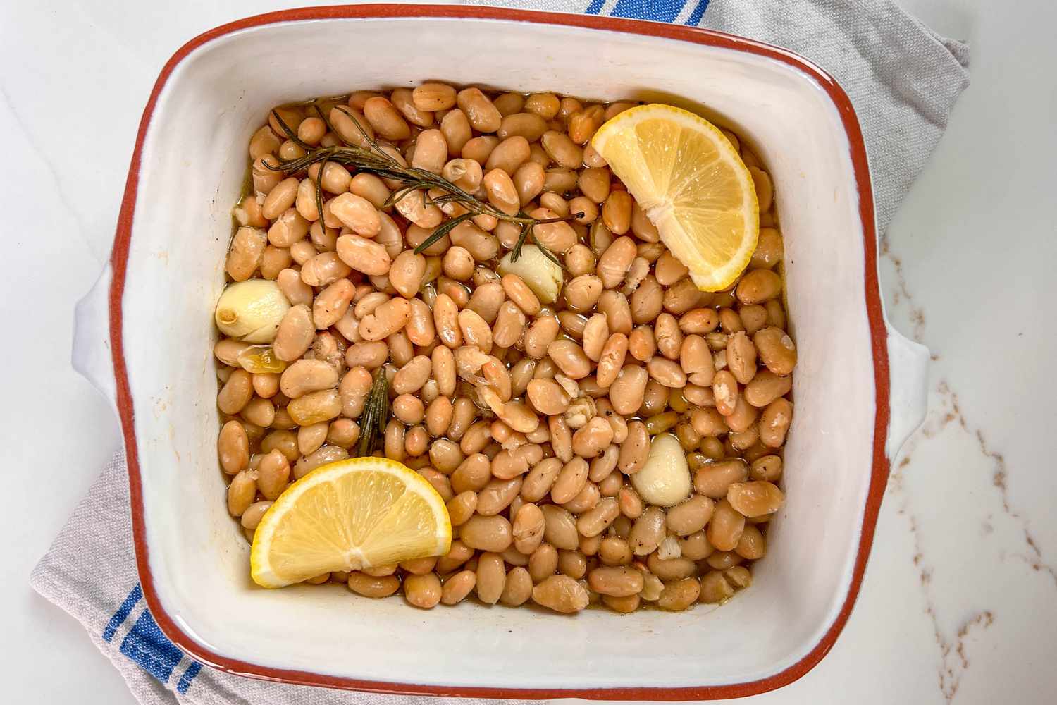 white beans, rosemary, garlic, and lemon in a white casserole dish