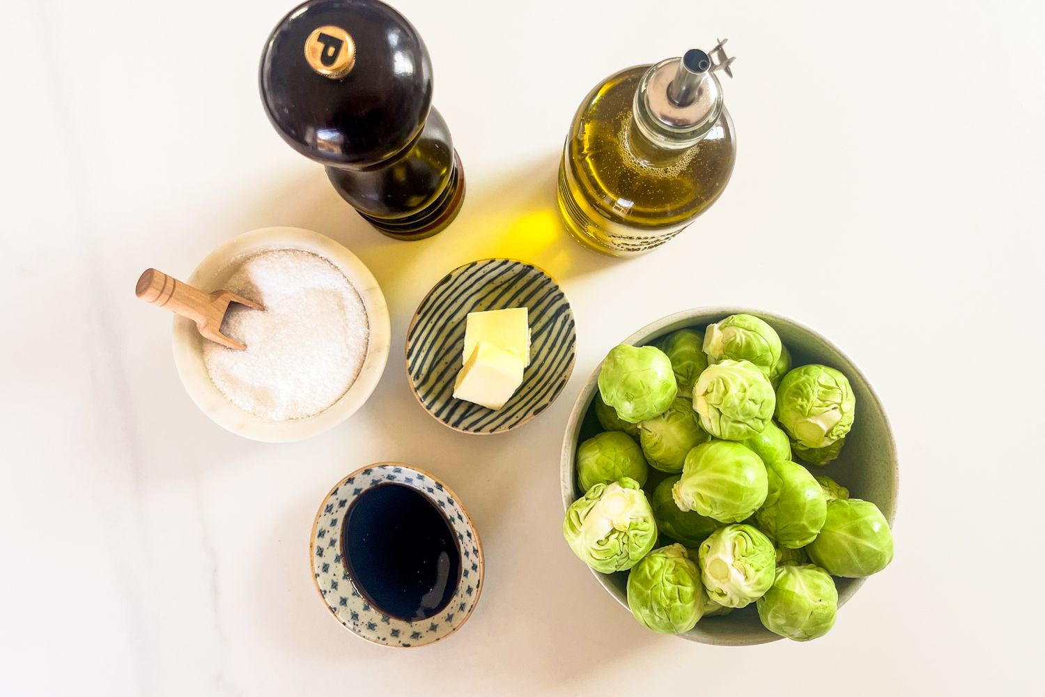 Ingredients including Brussels sprouts butter oil salt pepper and balsamic vinegar arranged on a surface