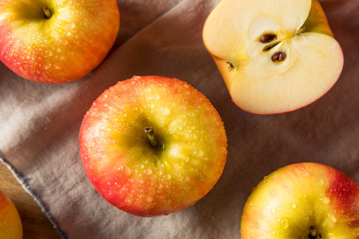 Crisp looking apples, crowned with water droplets that catch the sunlight; one apple is cut in half, showing the seeds in the core