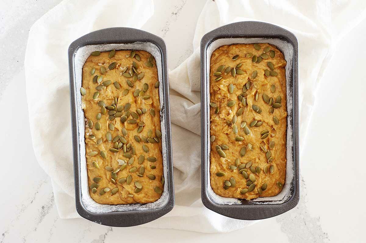 Overhead view of two Dairy-Free Pumpkin Bread batters in a loaf pans coated with parchment.