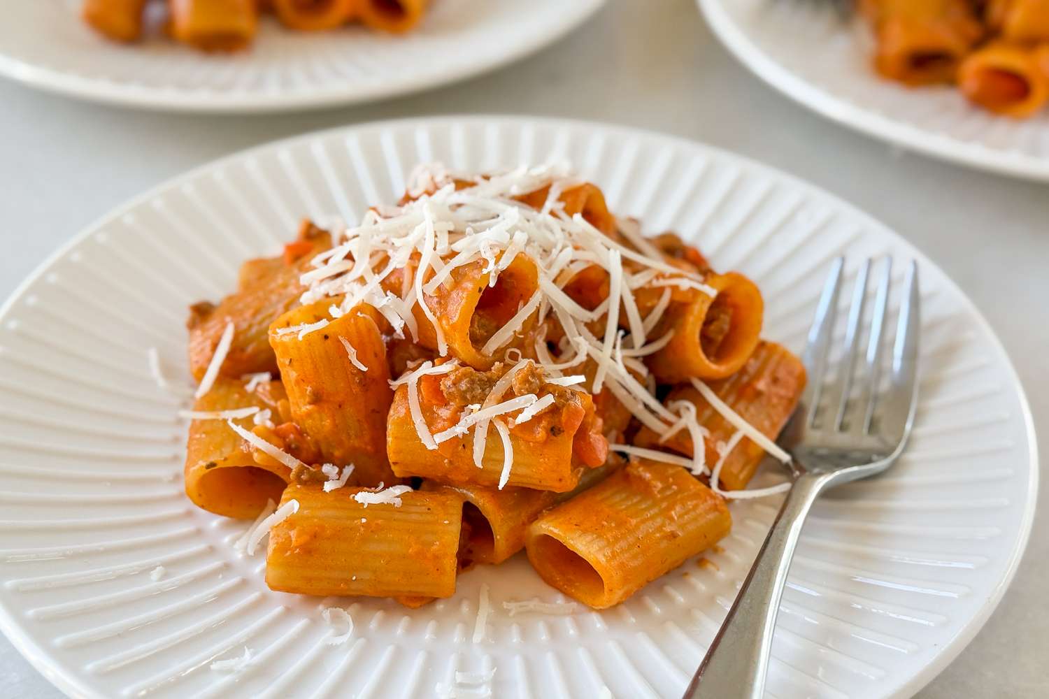 A plate of pasta with sauce and grated cheese served with a fork