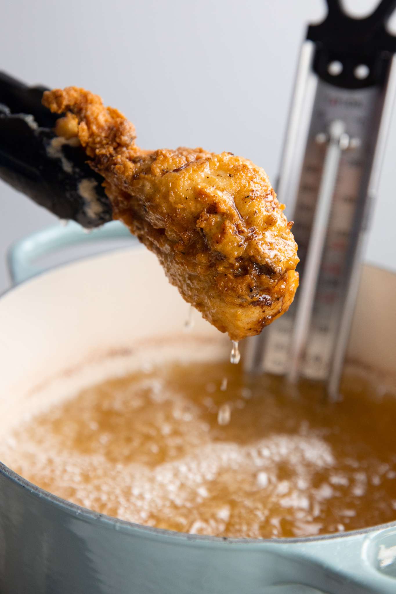 Piece of Fried Chicken Removed from Dutch Oven Filled with Oil Using a Pair of Tongs for How to Deep Fry 